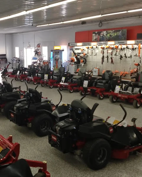 A photo of a showroom floor showcasing various brands of lawn mowers and yard tools.